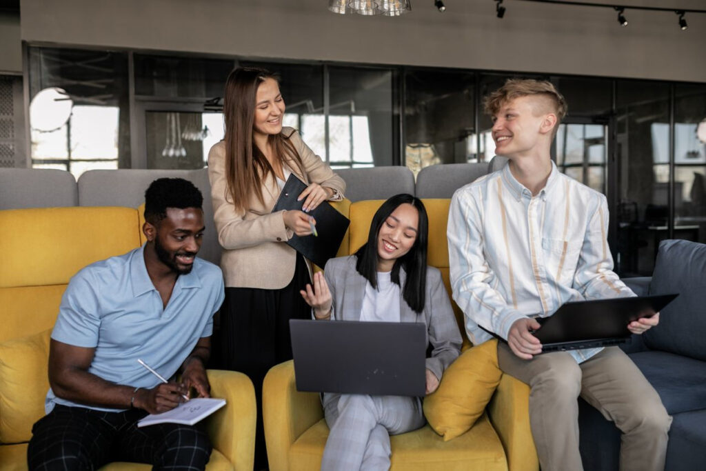 https://www.pexels.com/de-de/foto/manner-frauen-geschaft-business-7710046/ Gruppe von vier Personen, die auf Stühlen sitzen und an Laptops in einem hellen Raum arbeiten.