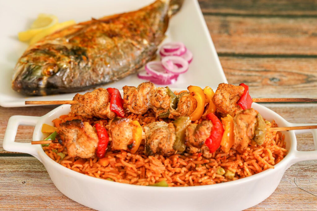 https://www.pexels.com/de-de/foto/gemuse-abendessen-mahlzeit-fisch-13915043/ Ein Teller mit gegrillten Spießen und Beilagen aus Reis, dekorativ angerichtet.