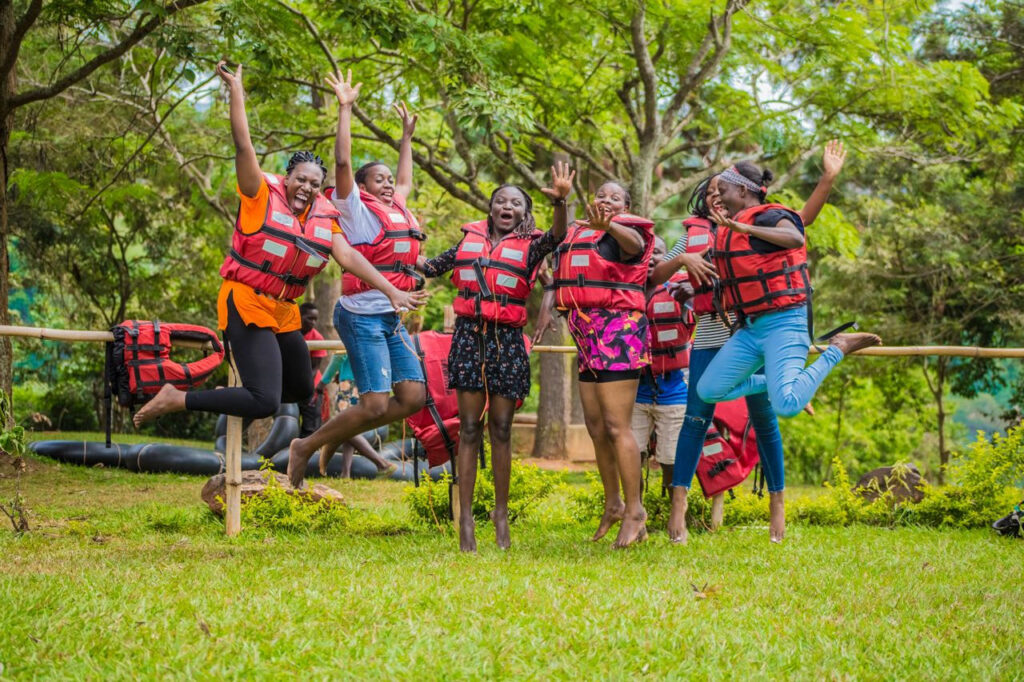 https://www.pexels.com/de-de/foto/freunde-springen-hupfen-frauen-18304835/ Mehrere Menschen in Rettungswesten versammeln sich auf einer Wiese.